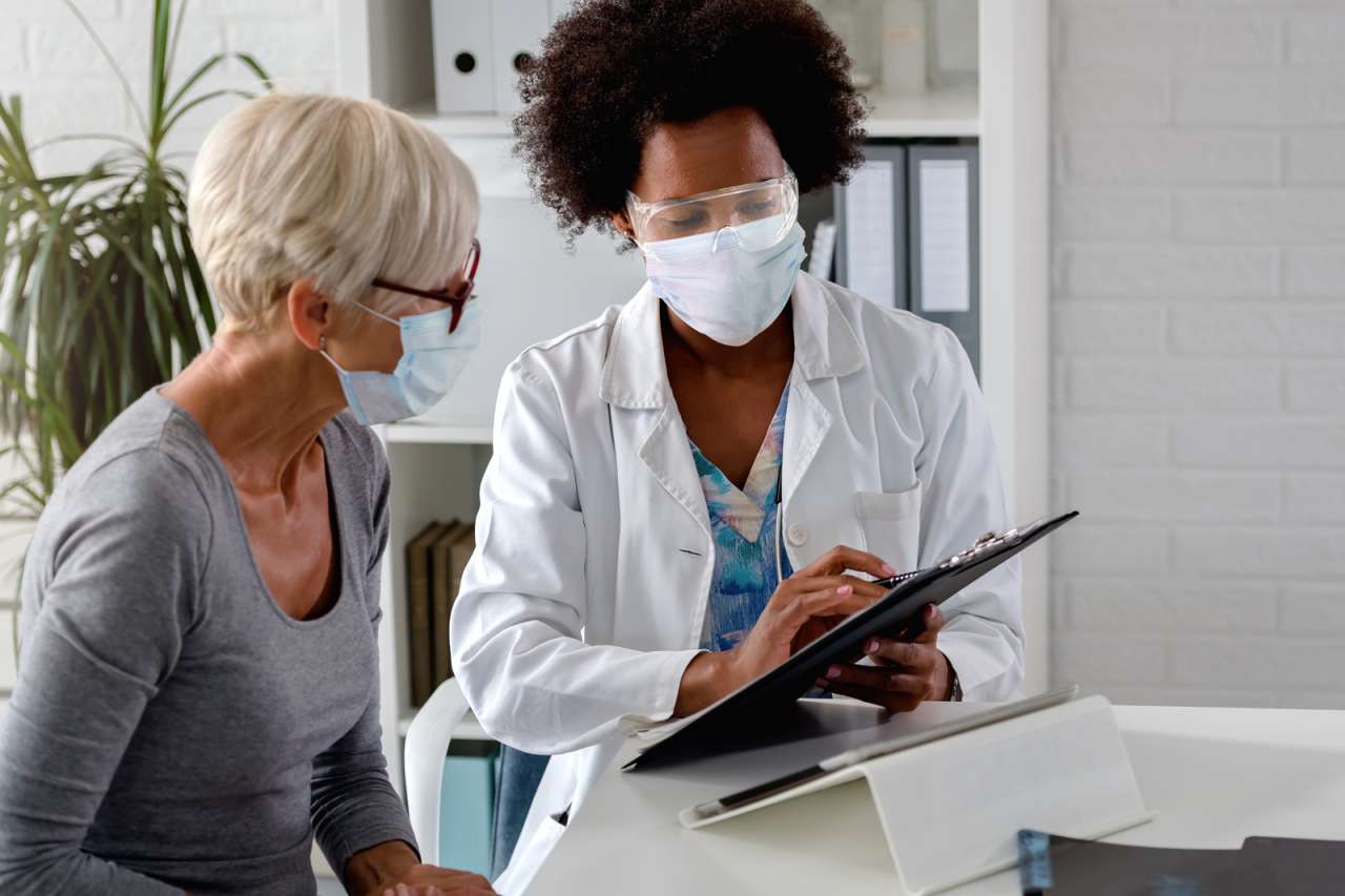 A black doctor with mask and face shield showing documents to a patient.