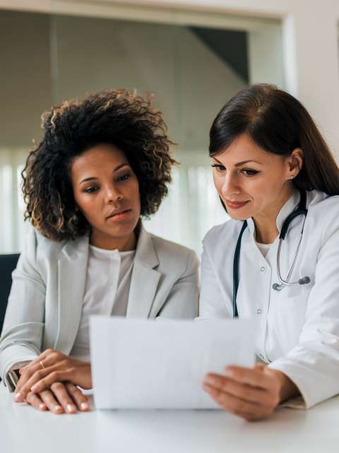 A doctor sitting next to and showing a document to a patient.